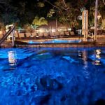 Piscina com água transparente e iluminação azulada, à noite.